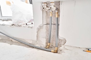 İnşaat halindeki yeni bir apartmanın beyaz radyatörüne bağlı ısıtma boruları. Su tesisatçısı olarak çalış. Beyaz duvarda su ısıtıcısı monte et.