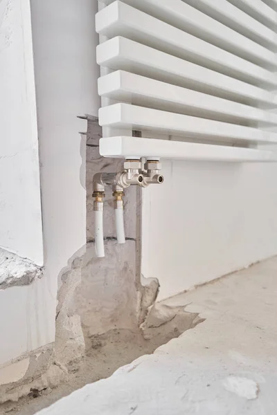 connection heating pipes to white Radiator in a new apartment under construction. Work As A Plumber, mounting water heating radiator on the white wall indoors