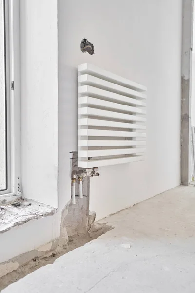 Conexión de tuberías de calefacción a radiador blanco en un nuevo apartamento en construcción. Trabaje como fontanero, montando radiador de calentamiento de agua en la pared blanca en el interior —  Fotos de Stock