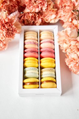 Çiçeklerin arka planında çiçekler olan bir kutuda makarna. Makarna kekleri ve farklı çiçeklerle dolu bir hayat.