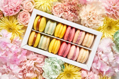 Çiçeklerin arka planında çiçekler olan bir kutuda makarna. Makarna kekleri ve farklı çiçeklerle dolu bir hayat.