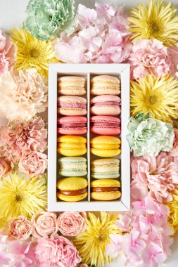 Çiçeklerin arka planında çiçekler olan bir kutuda makarna. Makarna kekleri ve farklı çiçeklerle dolu bir hayat.
