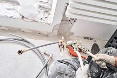 İnşaat halindeki yeni bir apartmanın beyaz radyatörüne bağlı ısıtma boruları. Su tesisatçısı olarak çalış. Beyaz duvarda su ısıtıcısı monte et.