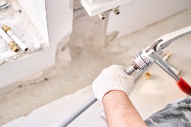 Tesisatçı, borunun istenen uzunluğunu makasla keser. İnşaat halindeki yeni bir apartmanın beyaz radyatörüne bağlanan ısıtma boruları.