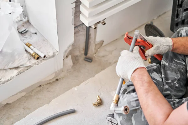 Rörmokaren skär den önskade längden av röret med saxverktyg. anslutning värmerör till vit radiator i en ny lägenhet under uppförande. — Stockfoto