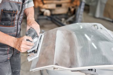 Tamirci öğütücü bir aletle çalışıyor. Araba parçalarının zımparalanması. Garaj boyama servisi. Kazadan sonra araba bölümü tamir ediliyor..