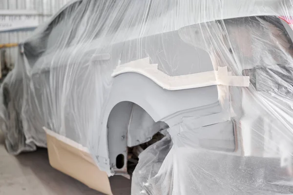 Garage painting car service. section of the car is covered with primer. vehicle is covered with protective paper. Repairing car body work after the accident by working sanding primer before painting.