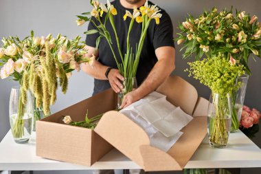 Adım adım, erkek bir çiçekçi bir karton kutuya çiçek koyar. Çiçek demeti, eve gitmek için hazır. Dekorasyon için taze kesilmiş çiçekler. Avrupa çiçekçisi. Taze kesilmiş çiçek getirdim..