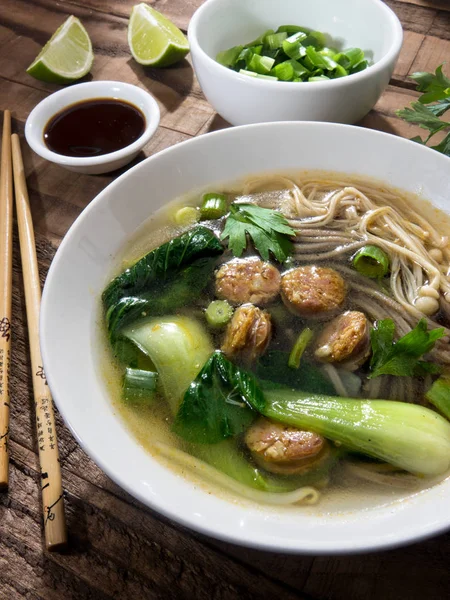 Chinese noodle soup with Chinese sausages and Japanese mushrooms on a wooden background