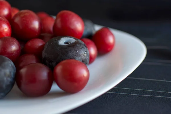 Taze erik ve kiraz eriği beyaz bir tabak ve siyah çizgili masa örtüsü