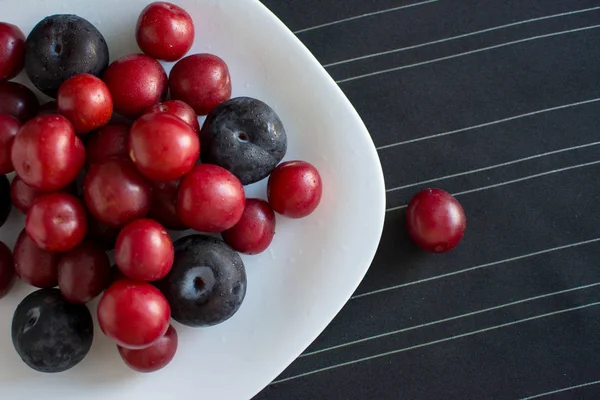 Fresh plums and cherry plum on a white plate and a black striped tablecloth