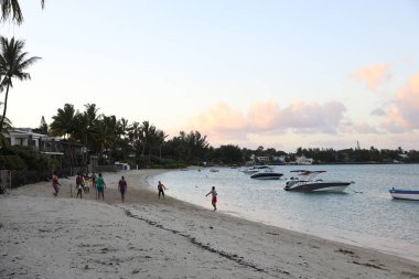 5 Mayıs 2018: Mauritius adasının sahilinde gün batımı, yatların suda yüzdüğü ve insanların sahilde oynadığı