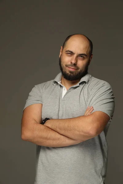 Portrait of a man with a beard who folded his arms in front of him and smiles. Gray background — Stock Photo, Image