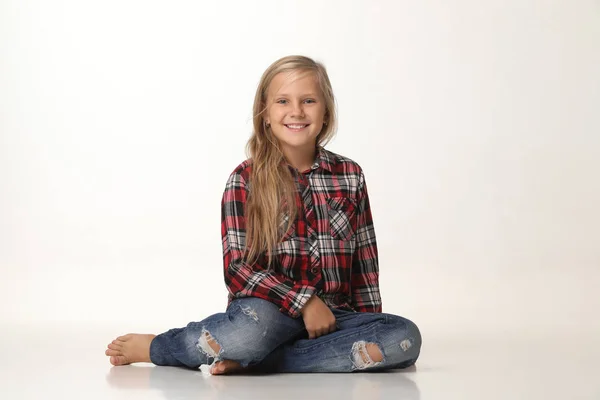 Menina bonito sentado no chão e sorrindo sinceramente. Fundo branco — Fotografia de Stock