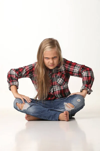 Dziewczyna z długimi blond włosami, z wyrażeniem zło siedzi na podłodze. Białe tło — Zdjęcie stockowe