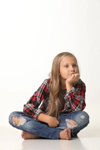 Menina com cabelo loiro longo senta-se no chão. Fundo branco — Fotografia de Stock