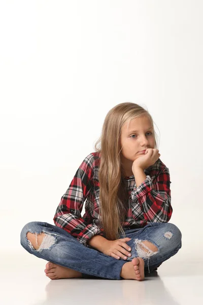 Flicka med långt blont hår sitter på golvet. Vit bakgrund — Stockfoto