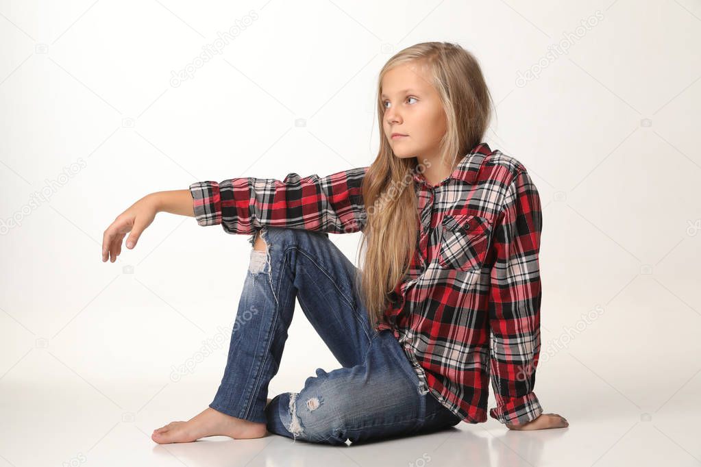 Girl with long blond hair sits thoughtfully on the floor. White background