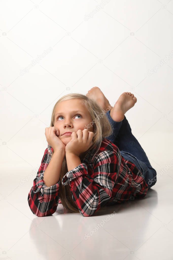Girl with long blond hair is lying thoughtfully on the floor. White background
