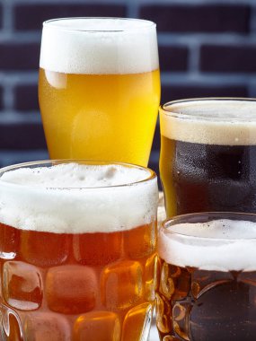 Bira ile dört bardak farklı renk ve çeşitleri, karanlık duvara karşı.