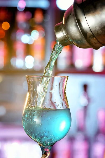 Barmen bir shaker dan mavi bir kokteyl bir çubuğu uzun bir bacak üzerinde güzel bir bardak içine dökülen güzel ışık ile bir bar counter.