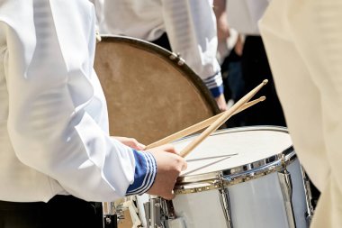 Closeup of a drummer in a brass band performing at a city park. Drum and wooden sticks. clipart