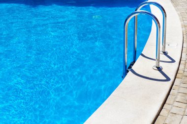 Güneşli bir günde otelin havuzunda yansıyan mavi su.