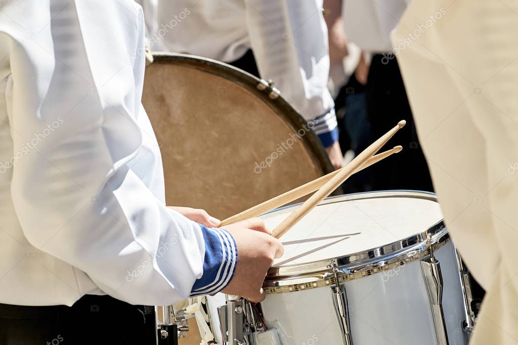 Closeup of a drummer in a brass band performing at a city park. Drum and wooden sticks.