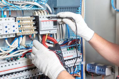 Elinde elektrik panel yanında duran bir tanı aracı ile üst düzey elektrikçi elektrik devreleri performansını ölçer.