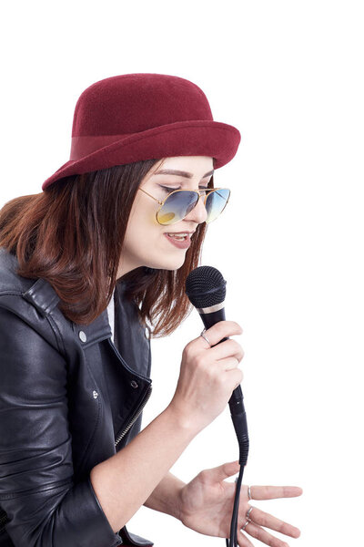 A young woman singing with a microphone wearing a white t-shirt and a red hat in a black leather jacket. Isolated on white background. Hipster style.