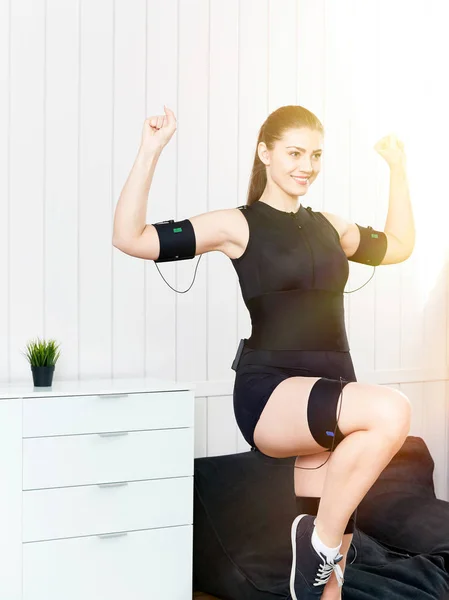 Beautiful young girl doing exercises on the machine for muscle stimulation. Innovative technology of exercise and fitness. Exercises for women on the electro-muscular machine.