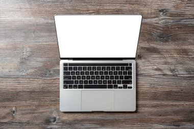 Güzel ahşap bir masada beyaz ekranı olan modern bir dizüstü bilgisayarın üst görüntüsü. Tasarım şablonu.