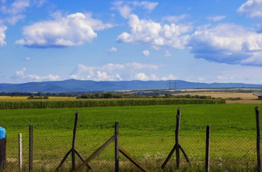 Dağlar ve mavi gökyüzü bulutlu arka planda çitlerle çevrili alanlar