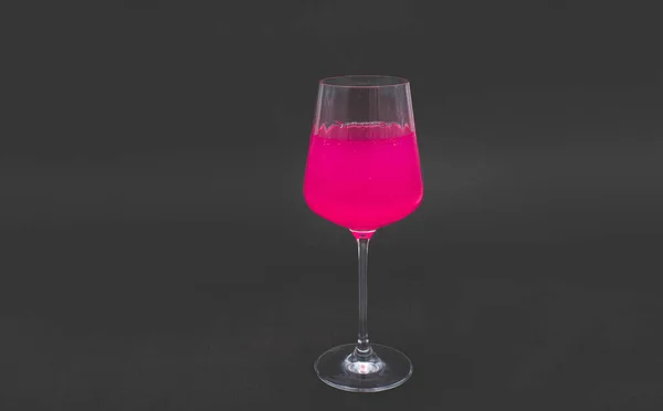 Pink drink in wine glass. On a black background