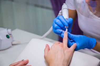 Güzellik salonundaki donanım manikürünü yakından çek. Manikürcü kadın parmaklarına manikür yapmak için elektrikli tırnak matkabı uyguluyor..