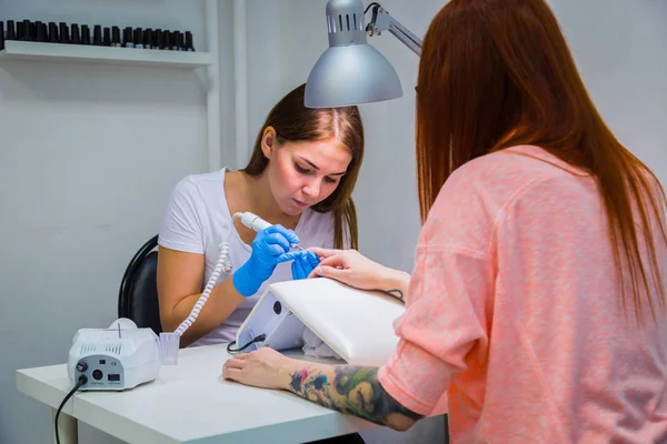 Woman in a nail salon receiving a manicure by a beautician with electric nail file. Woman getting nail manicure. Beautician file nails to a customer