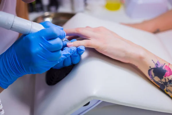 Closeup shot of hardware manicure in a beauty salon. Manicurist is applying electric nail file drill to manicure on female fingers.