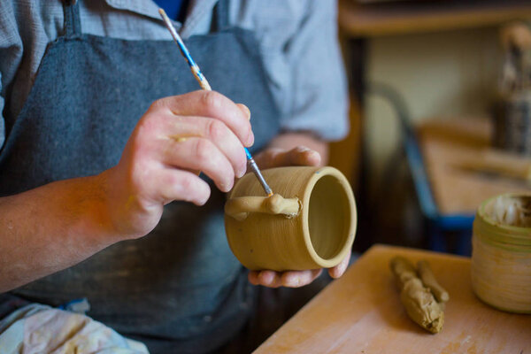 Professional potter making pattern on clay mug with special tool in pottery