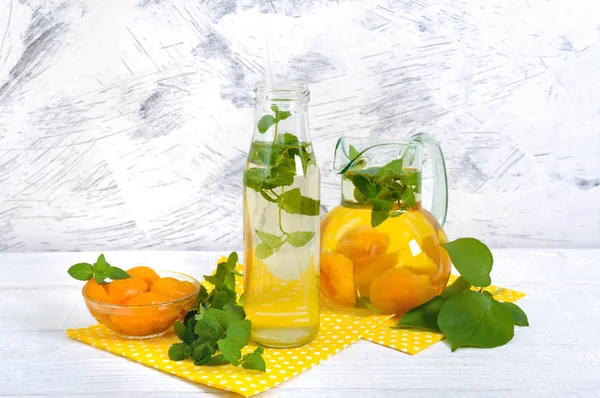 Summer cold drinks. Delicious refreshing drink with apricot and mint in glasses on a white wooden background. Compote of fruits.