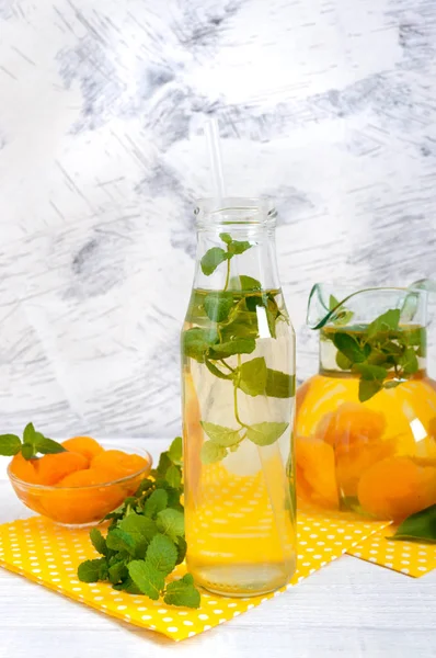Summer cold drinks. Delicious refreshing drink with apricot and mint in glasses on a white wooden background. Compote of fruits.