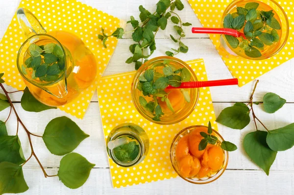 Summer cold drinks. Delicious refreshing drink with apricot and mint in glasses on a white wooden background. Compote of fruits. The top view