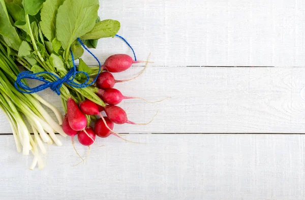 Taze kırmızı turp ve beyaz ahşap zemin üzerine yeşil genç soğan. Sağlıklı beslenme ile turp. Bir ışık bahar sebze salatası için malzemeler. Bir yazıt için boş alan.