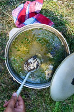 Balık çorbası kaynar kazan niteliğine tehlikede içinde. Çorba ateşte bir tencerede. Üstten görünüm. Elini balık bir parça bir kaşık ile alır..