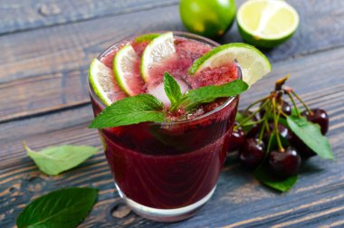 Ahşap bir masa üzerine nane yaprakları ile süslenmiş yaz vitamin içeceği kiraz, limon, buz. Meyve kokteyli. Yakın çekim.