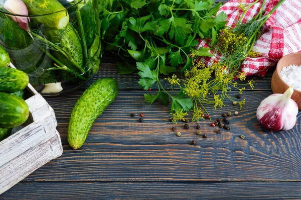 Pickles. Delicious pickled cucumbers in a jar, fresh harvest in a wooden box, spices, herbs on a table. Preparation of cucumbers for pickles.