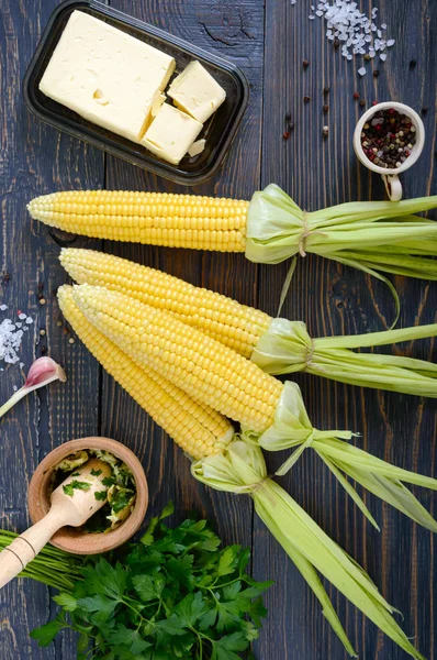 Ham şeker Mısır, deniz tuzu, baharatlar, bitkiler, koyu ahşap masa üzerine tereyağı. Üstten görünüm.
