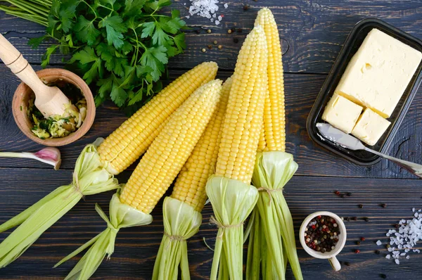 Ham şeker Mısır, deniz tuzu, baharatlar, bitkiler, koyu ahşap masa üzerine tereyağı. Üstten görünüm.