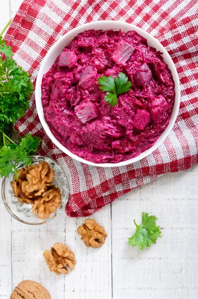 Delicious salad with boiled beets, herring, nuts, onions in a white ceramic bowl. Top view.