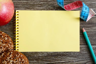 Sağlıklı beslenme kavramı. Diyet simge - elma, tahıl kurabiye ve notlarınızın bir yere ortasında ahşap bir arka plan üzerinde ölçüm bandı. Üstten görünüm.