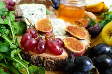 Meze çeşitleri: üzüm, peynir, mavi peynir, incir, kavun, roka, tahıl ekmeği, tatlım ahşap bir masa üzerinde bir yuvarlak ahşap tepsi